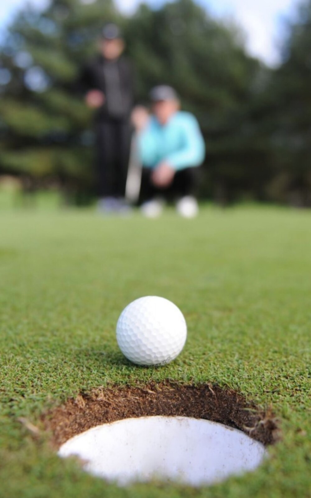 Golf ball resting just behind the hole as two golfers read the green